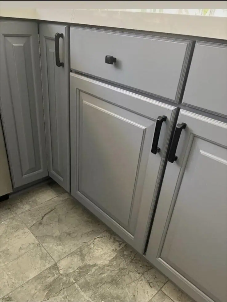 Gray kitchen cabinets with black handles and a white countertop.